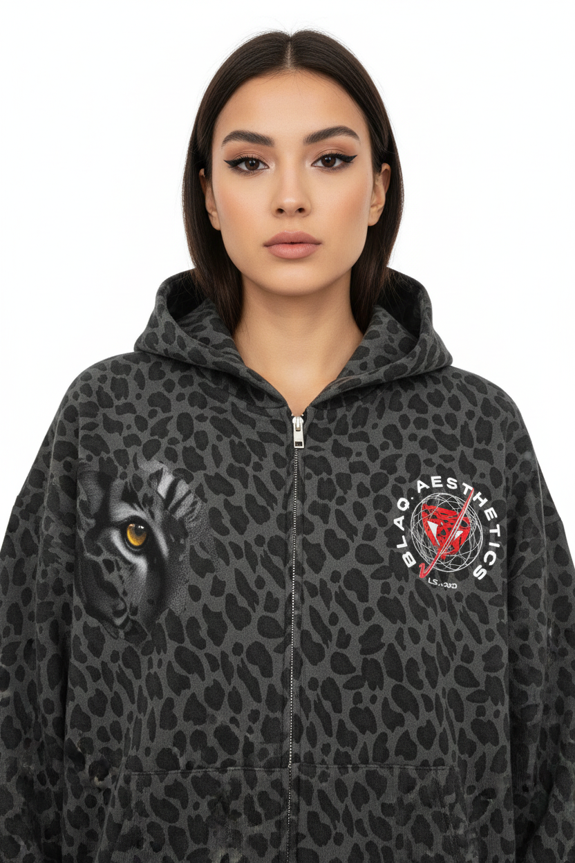 A woman wearing a dark gray and black leopard-print zip-up hoodie with a graphic of a black cat's face on the left chest and a circular 'Black Aesthetics' logo on the right chest.