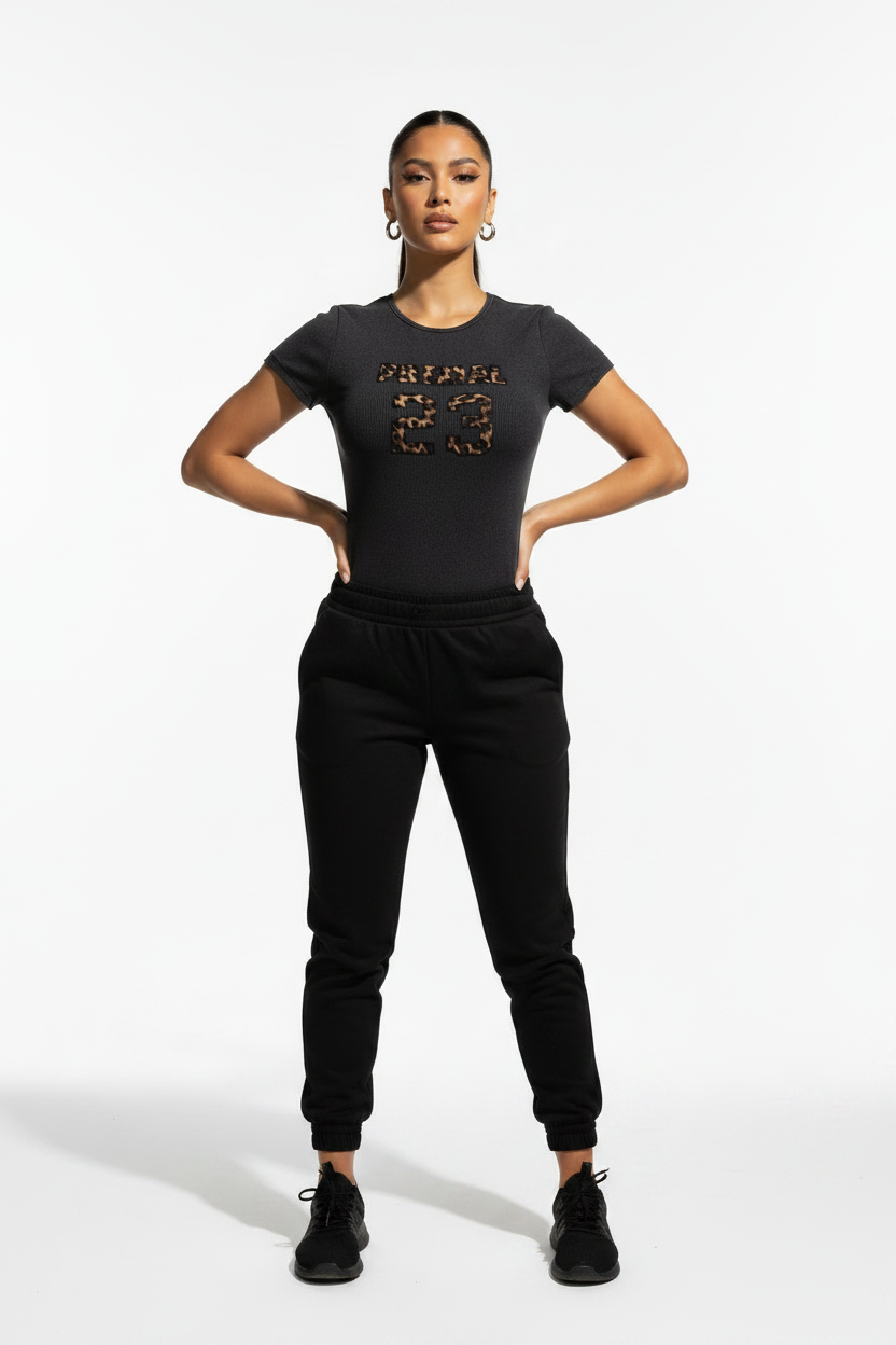 A model stands against a light gray studio background wearing a black short-sleeve bodysuit with a leopard-print graphic on the chest.